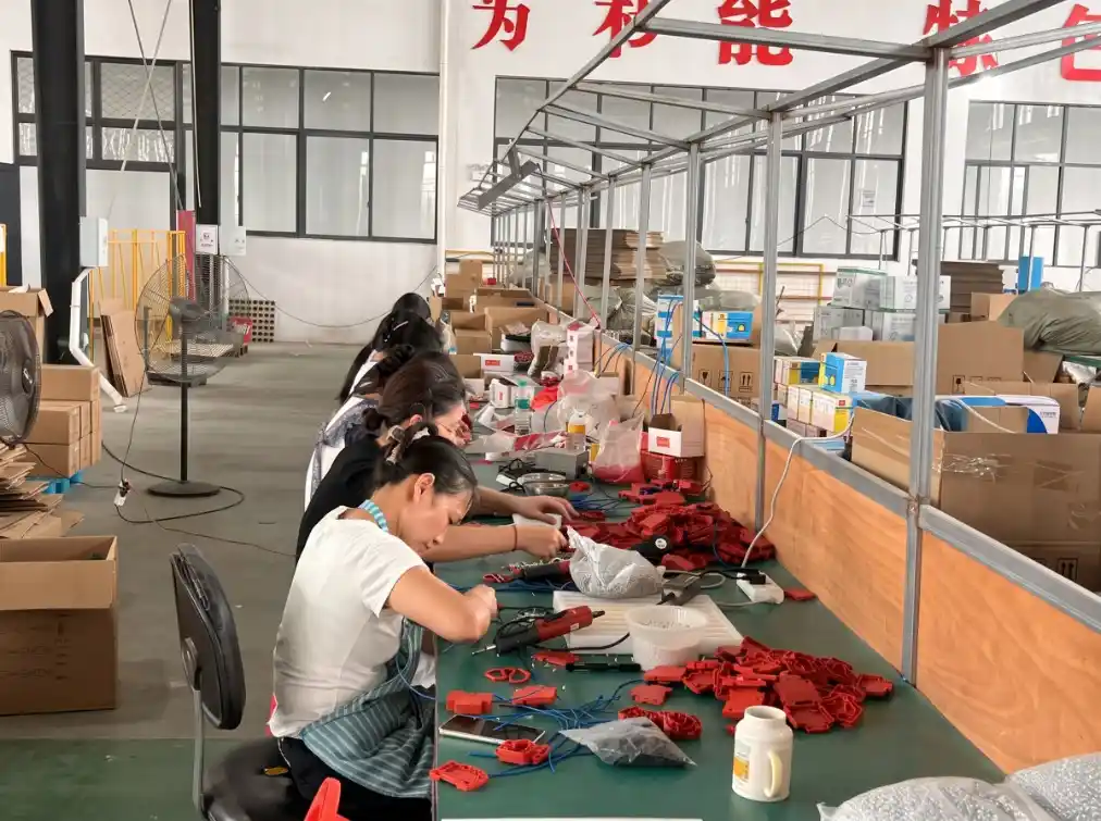 Workers assembling red product housings and wiring at a production workbench
